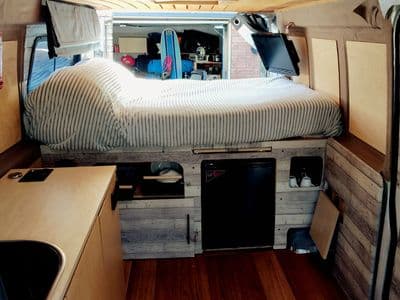 Hand-built interior of The A Van with double bed, kitchen and fridge