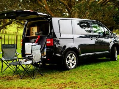 Mitsubishi Delica sleeper van with open tailgate kitchen and camping chairs