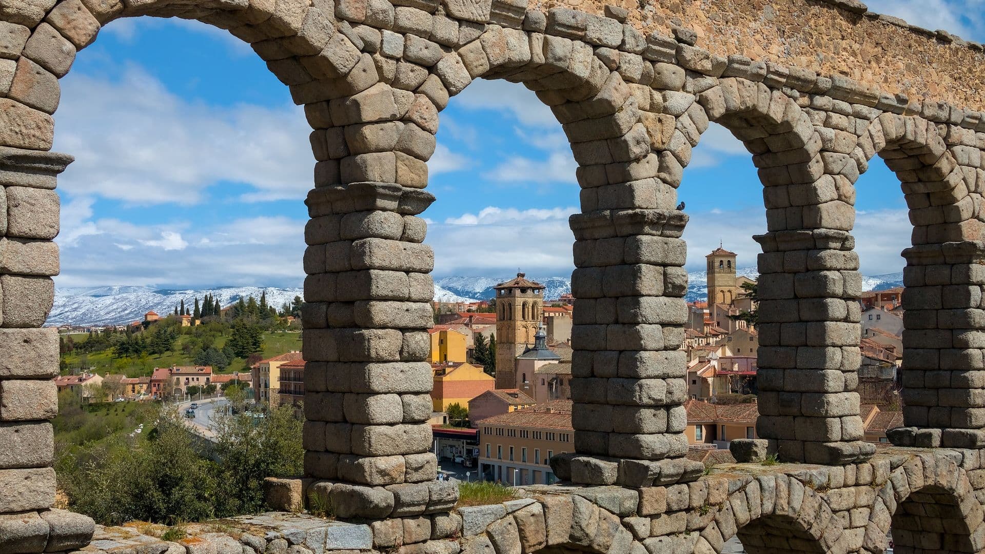 Roman aqueduct of Segovia with the old town and the snow-covered Sierra de Guadarrama behind it, a day trip from Madrid