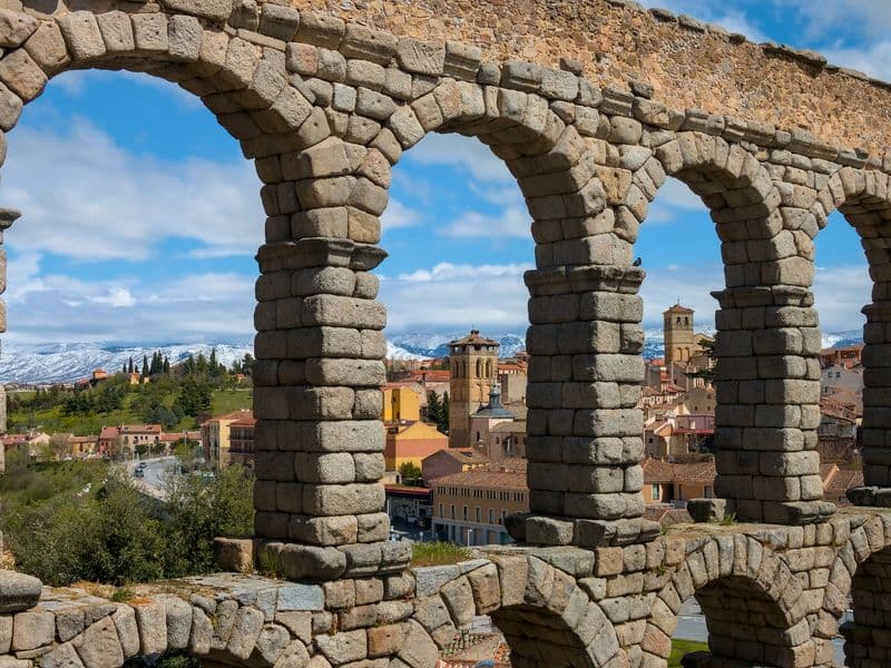 Roman aqueduct of Segovia with the old town and the snow-covered Sierra de Guadarrama behind it, a day trip from Madrid